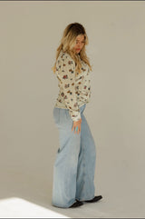 Woman wearing a floral blouse and light blue pants against a plain background