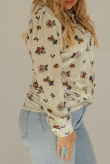 Woman wearing a floral long-sleeve top and light blue jeans against a plain background