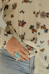 Close-up of a hand wearing a turquoise ring on a floral-patterned shirt.