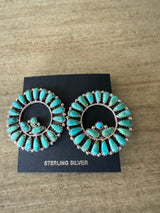 Turquoise earrings on a black card with 'STERLING SILVER' text, placed on a wooden surface.
