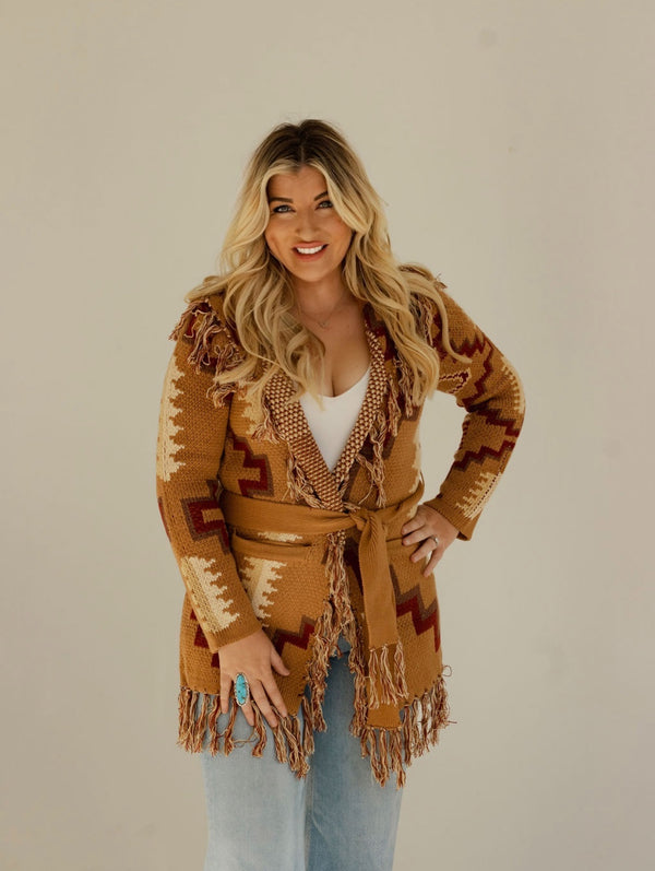 Woman wearing a patterned brown cardigan with a belt against a plain background